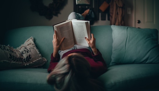 woman lying on sofa reading book